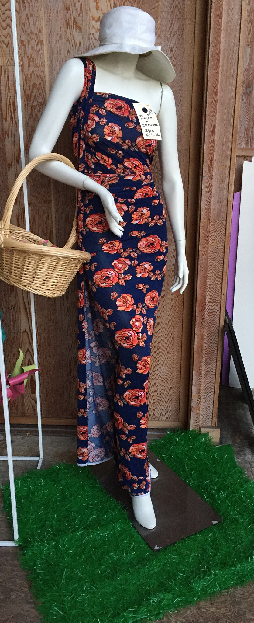 Floral rayon knit fabric draped over a store mannequin with a basket hanging from right arm and a white summer hat.